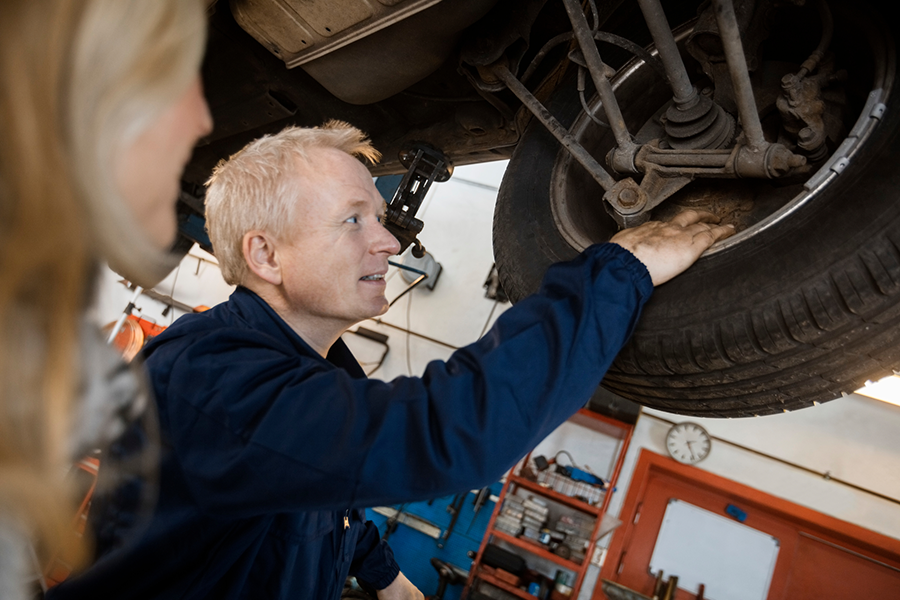 Person in coveralls inspecting the tire well of a vehicle up on a lift