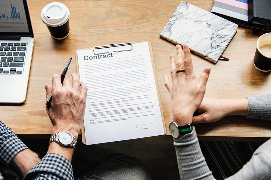 The hands of two people at a table with a contract on a clipboard between them
