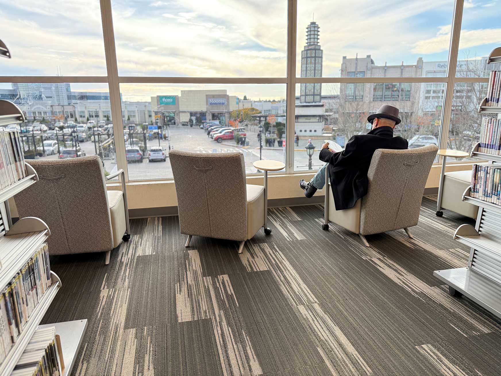 Interior shot of Emily Carr branch showing large windows. Someone is sitting in a chair reading while enjoying the view