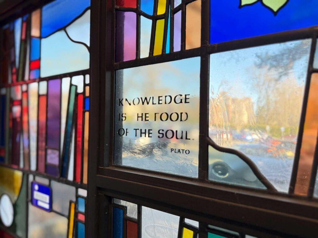 stained glass of books detail - there are words on one pane that say "knowledge is the food of the soul - Plato"