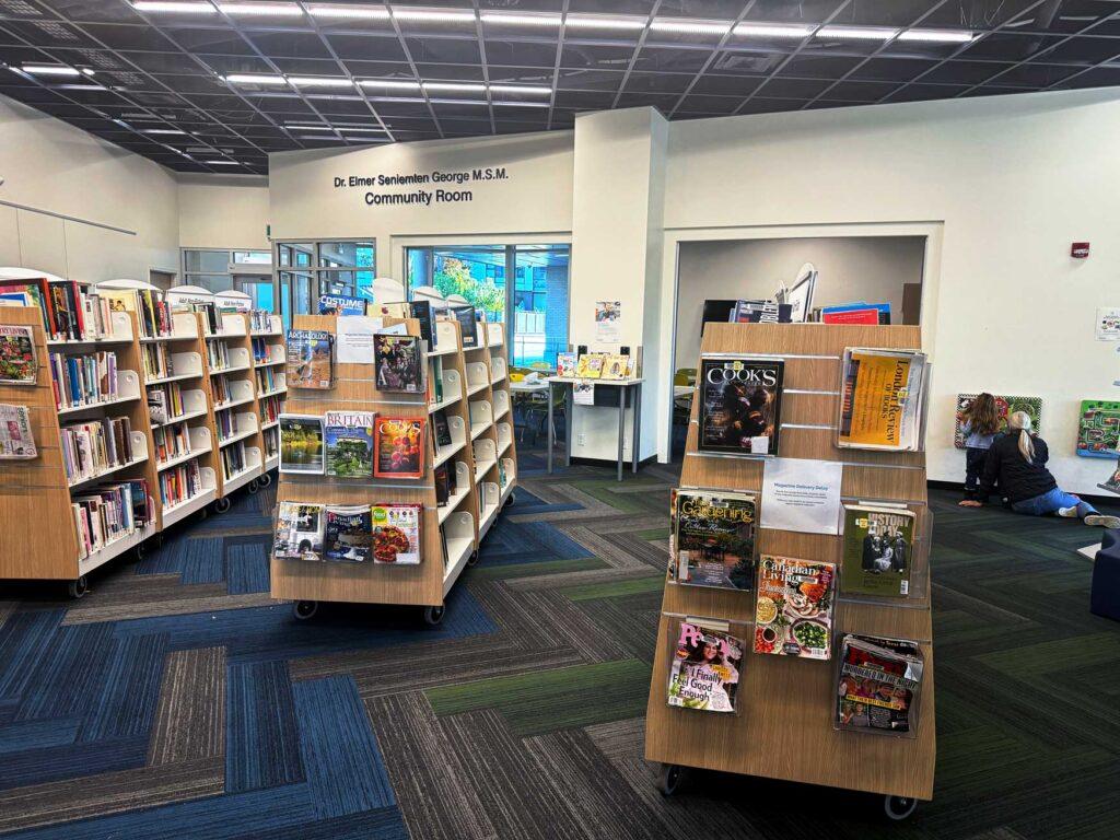 indoors of SJB branch - bookshelves are seen on a zigzagged carpet. On the wall in the background the words "Dr. Elmer Seniemten George M.S.M. Community Room" can be seen