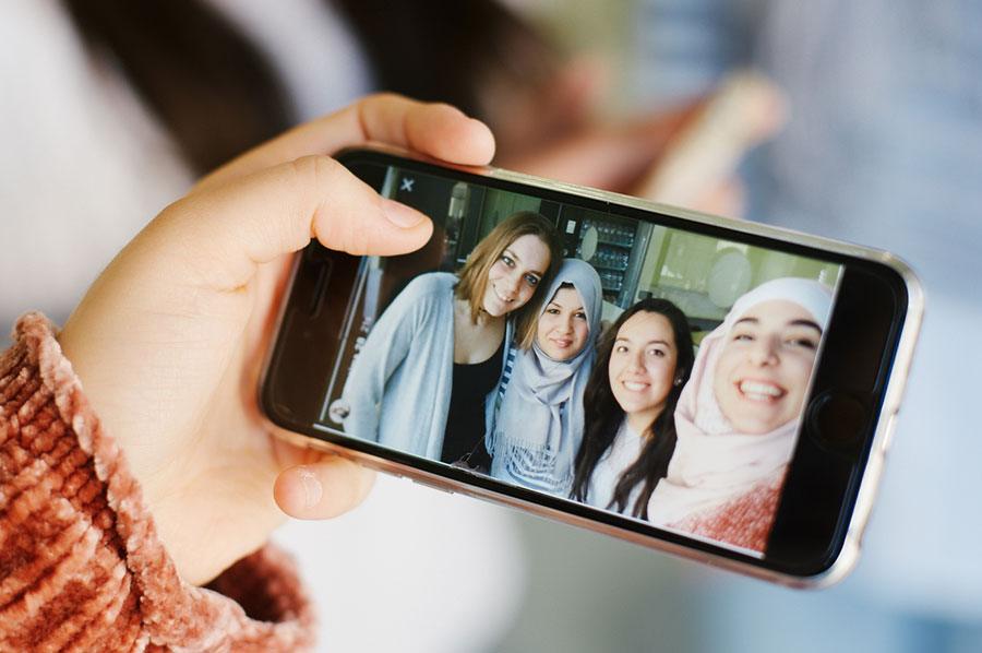 a hand holds a phone with an image of 4 smiling women displayed