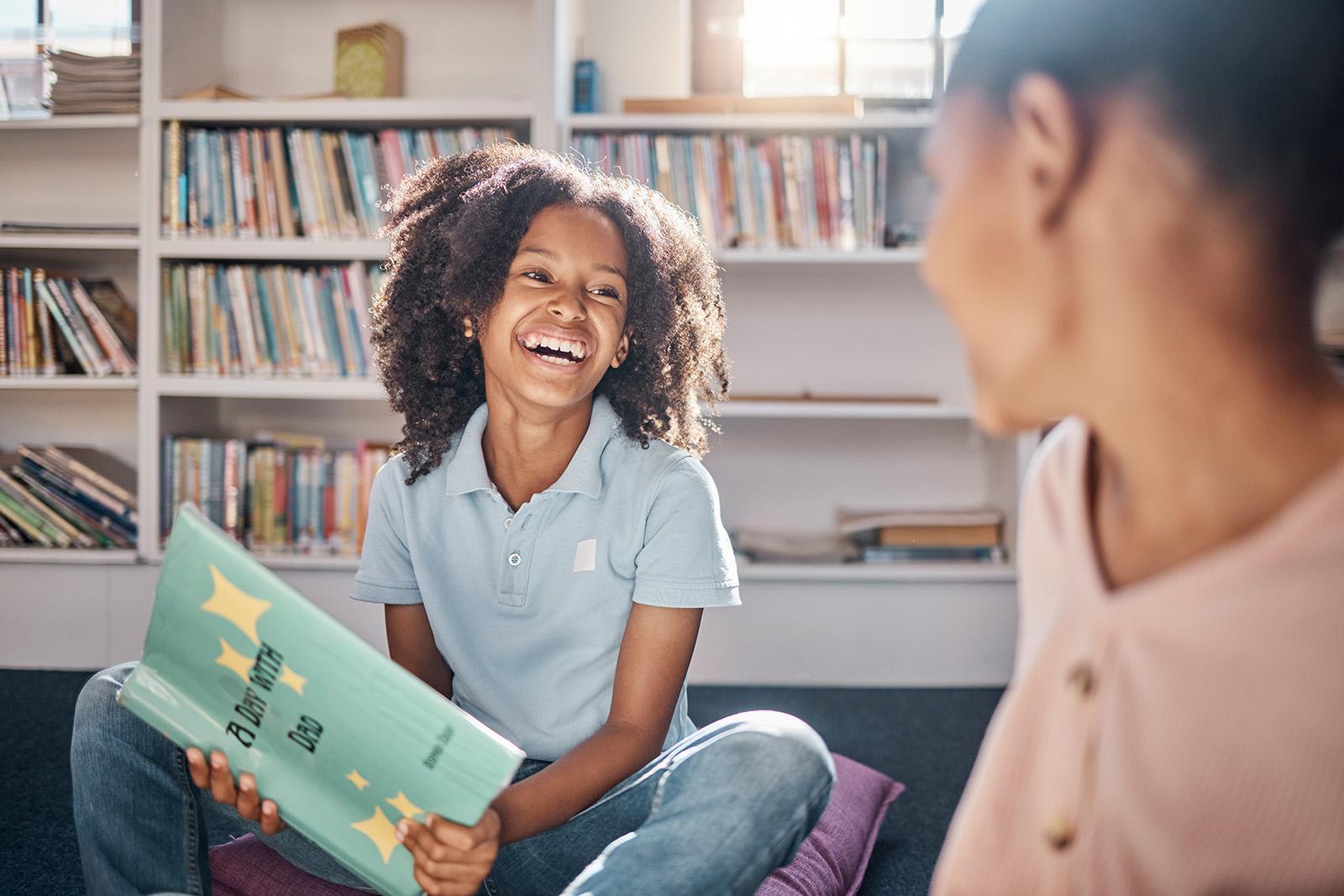 girl and mom laughing in the library - the girl is holding a book