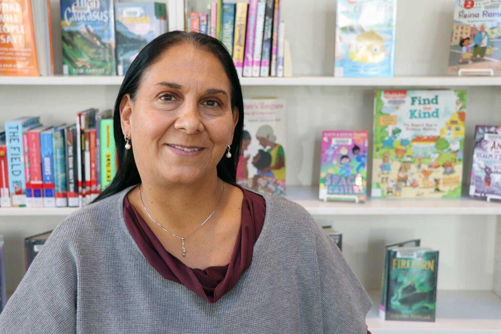 an indigenous woman stands in front of a shelf stacked with books on display