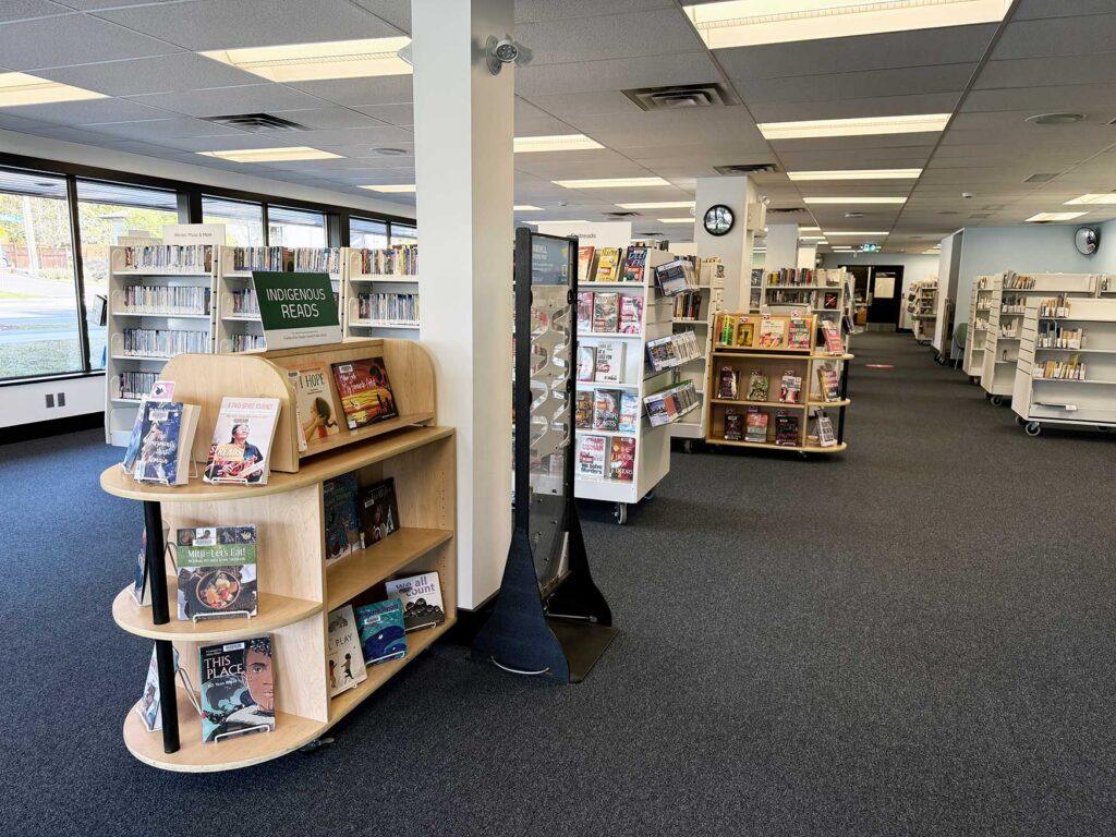 Nellie McClung Express branch interior - rows of bookstacks. a shelf in the front of the picture shows a sign on top that states that it is featuring "indigenous reads"