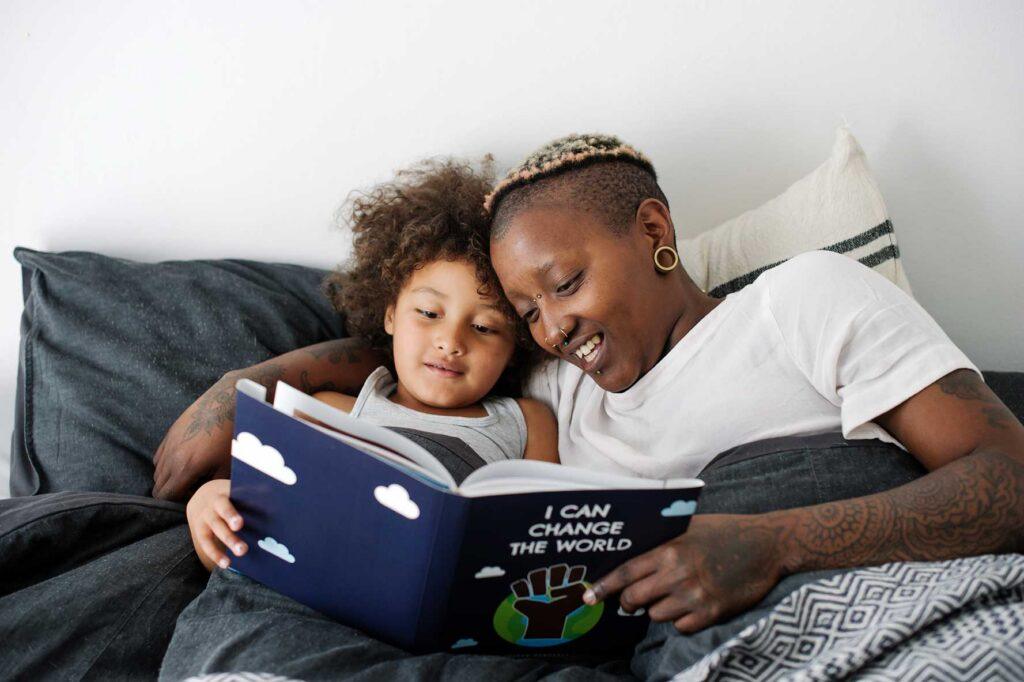 a young girl and a woman are curled up on a couch reading a book together