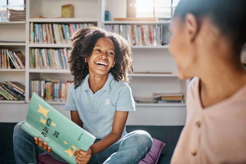 happy child looking at an adult who is reading to her in the library