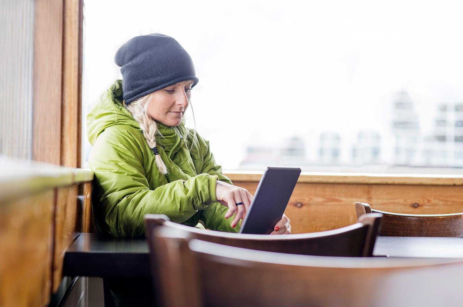 a woman wearing a jacket and toque works on a tablet near a window
