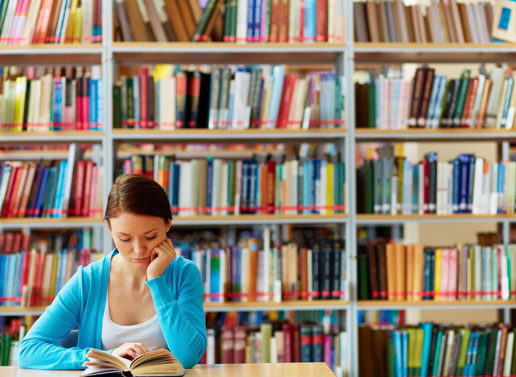 young women reading in the library - many books are seen behind her