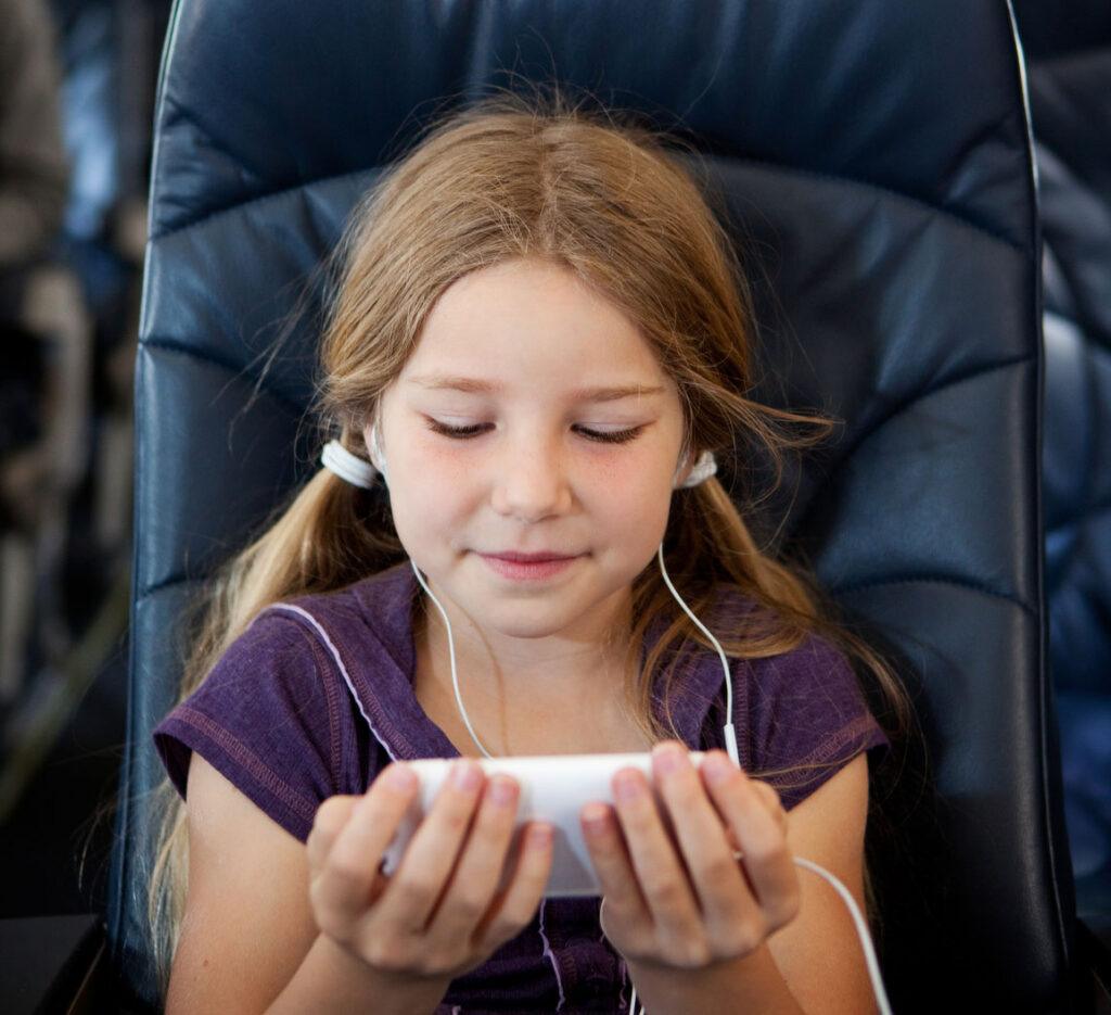 Young girl in a chair, with ear pods and watching her tablet screen.