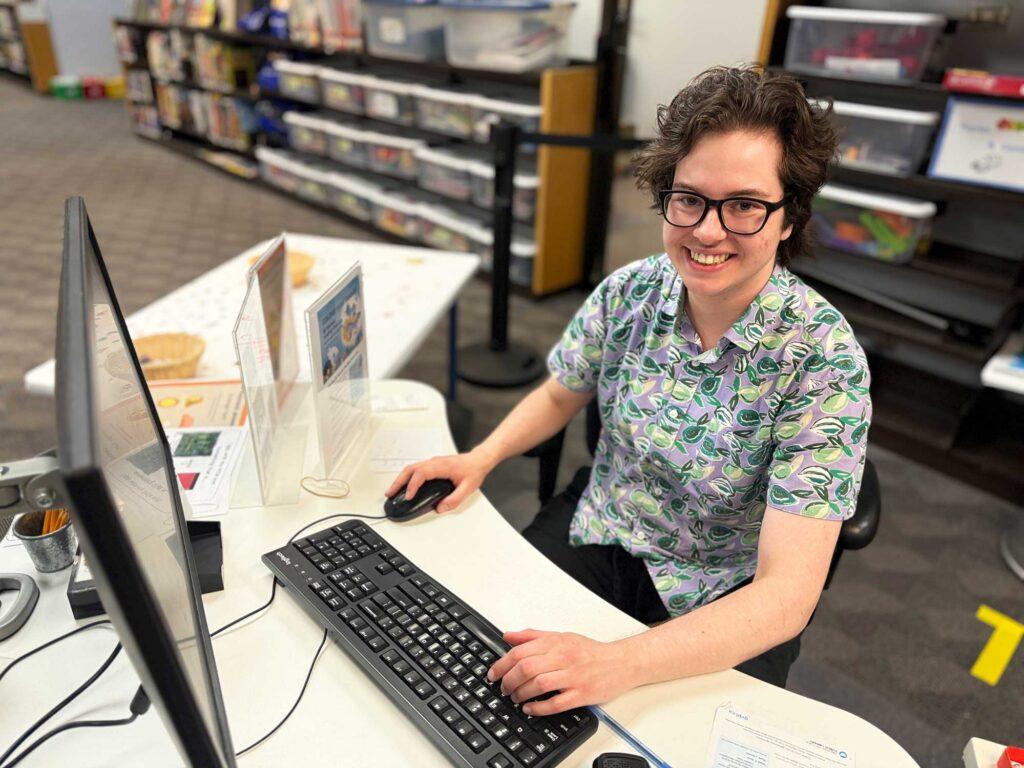 Library staff smiling at desk with hands on keyboard.