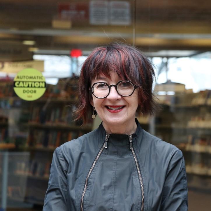 Woman with short dark hair wearing jacket with backdrop of library shelves