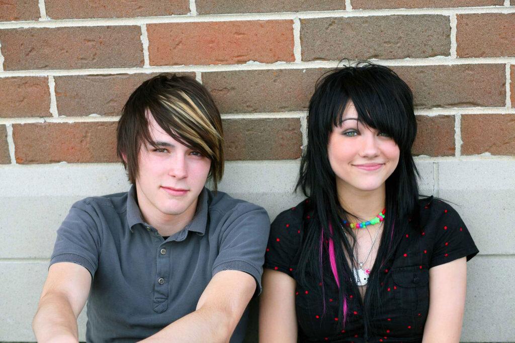 Teenage boy and girl sitting outside, grinning.