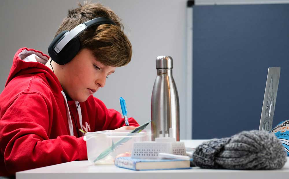 Teen studying at laptop wearing headphones.