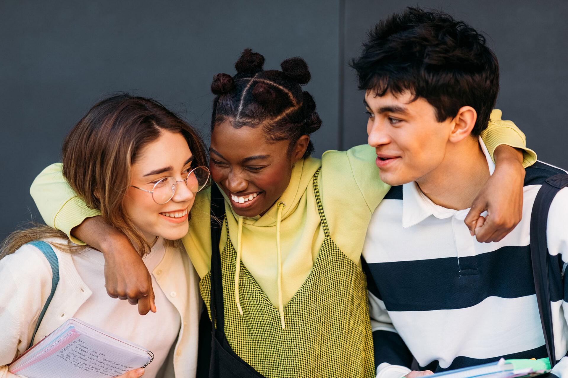 Three young students, hugging and laughing.