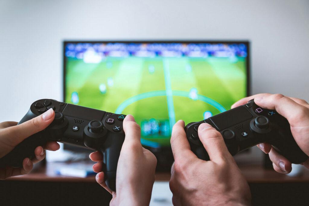 Two sets of hands holding xbox controllers playing a video game of soccer.