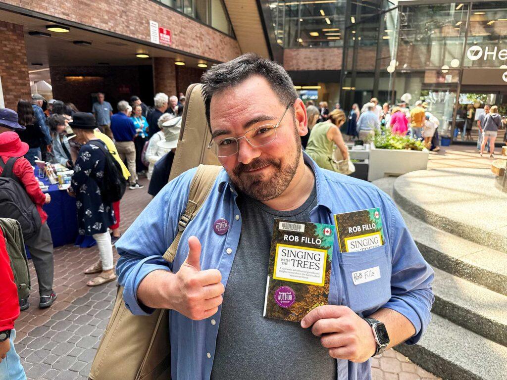 Emerging Local Author proudly holding his book in front of crowd at collection launch event in Central Branch courtyard.