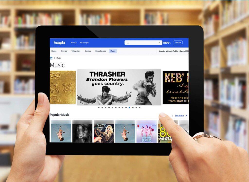 Hands holding a tablet selecting from Hoopla popular music options. 