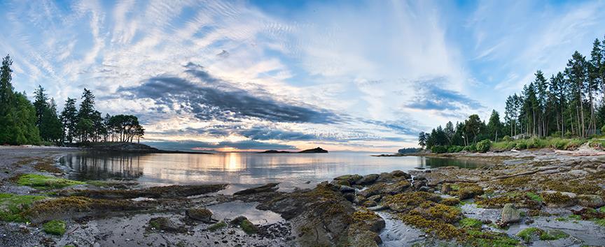 Coastal scenery with rocky shoreline, trees on either side and a dramatic cloudy sky.