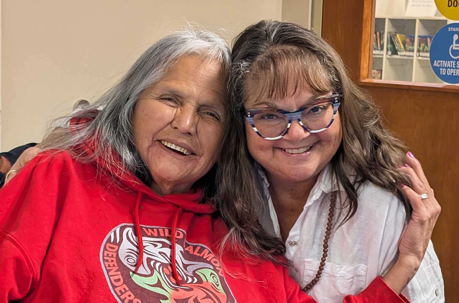 Two ladies smiling with their heads touching.