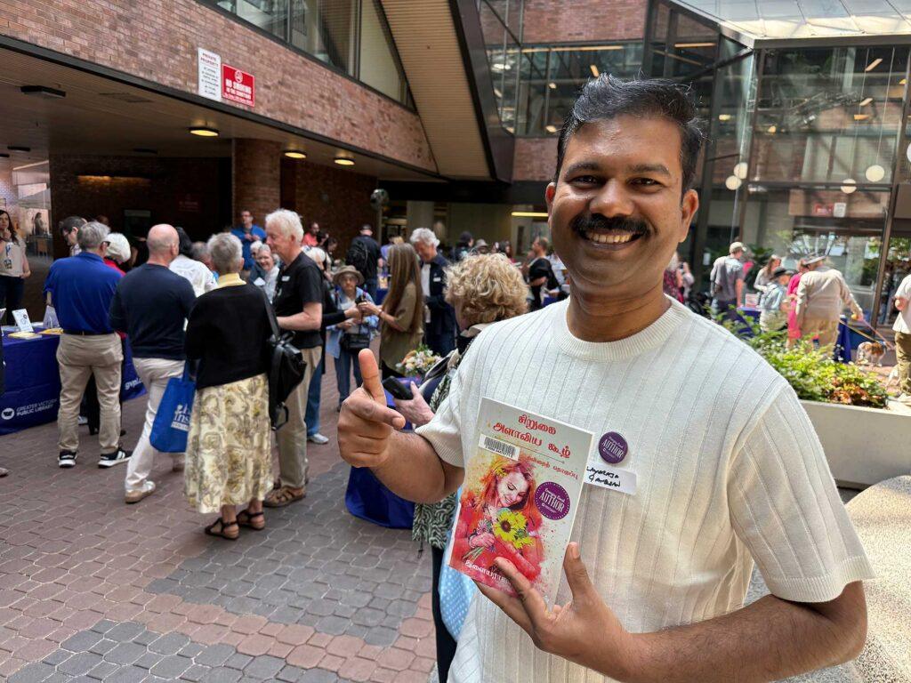 Smiling Emerging Local Author holding book with thumbs up.