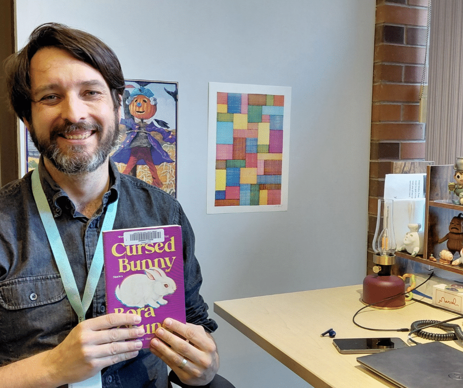 Man sitting at his desk holding up book